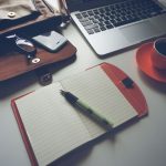 un bureau avec ordinateur, cahier, tasse de café et sac