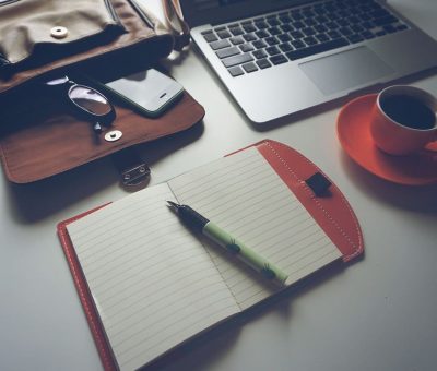 un bureau avec ordinateur, cahier, tasse de café et sac
