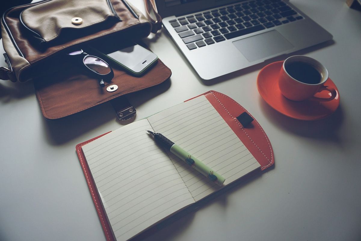 un bureau avec ordinateur, cahier, tasse de café et sac
