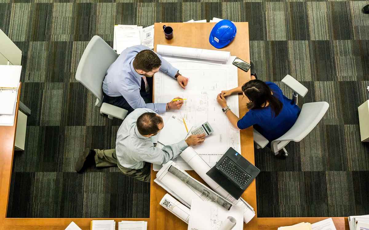 Trois collaborateurs étudient des plans sur une table de travail