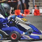 Un coureur en karting porte un casque et pilote un kart bleu sur piste