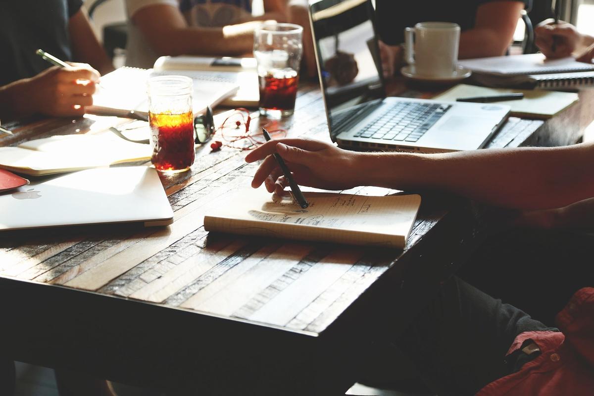 Une main écrit dans un carnet sur une table en bois