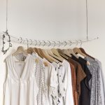 Une rangée de cintres suspendus portant des vêtements légers sur un mur blanc